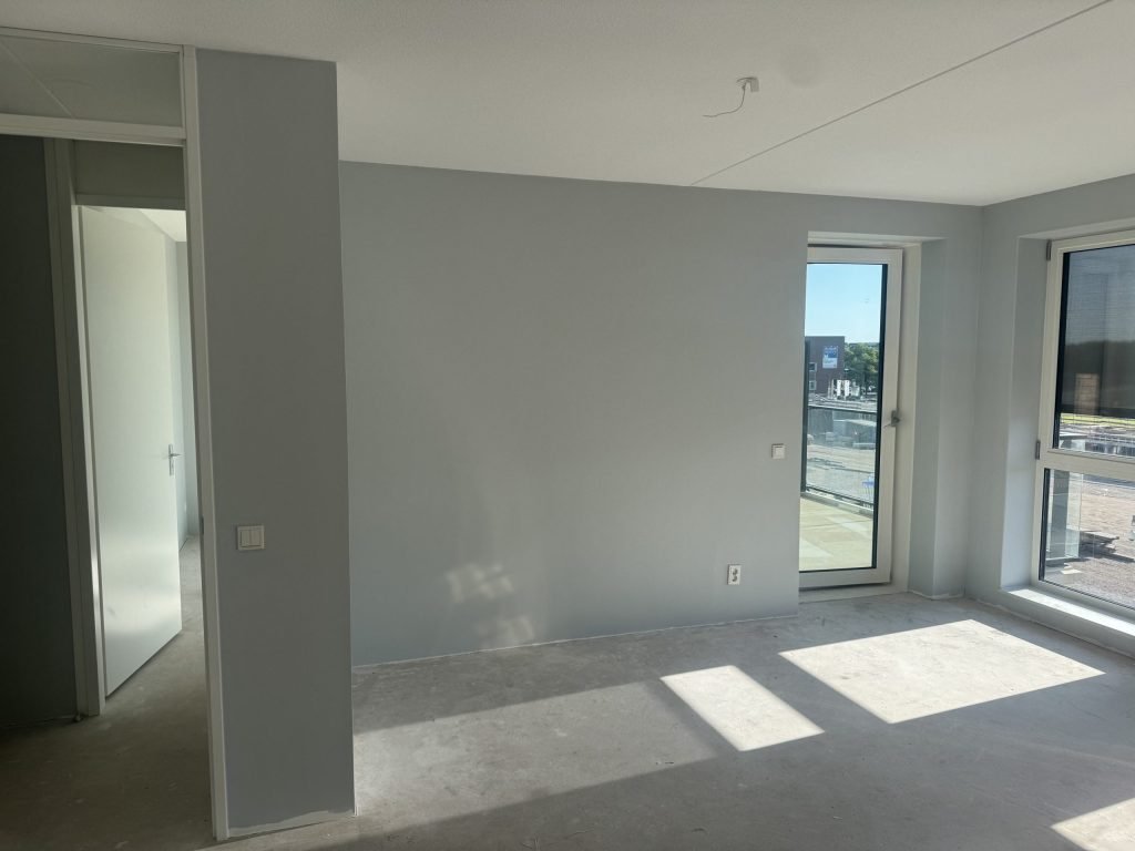 Pas opgeleverd appartement met balkondeur, lichte wanden en een kale betonvloer