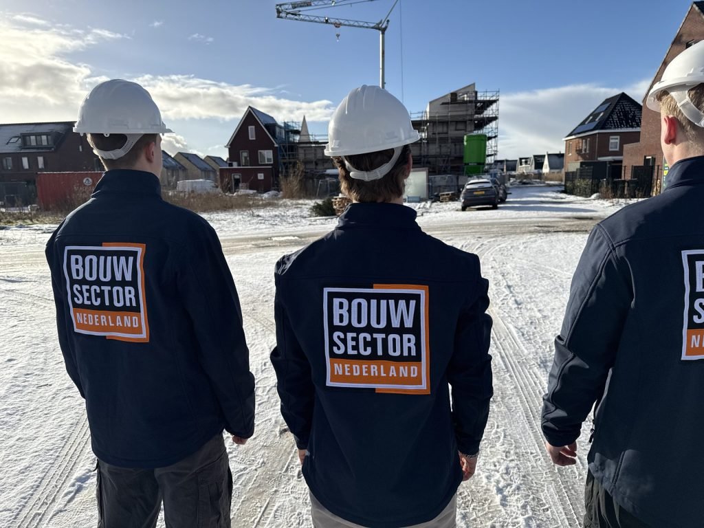 Drie vakmensen van Bouwsector Nederland met witte helm bij een nieuwbouwwijk met hijskraan